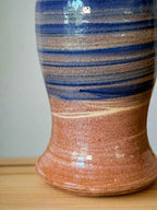 Ceramic vase with blue and brown stripes on a wooden surface